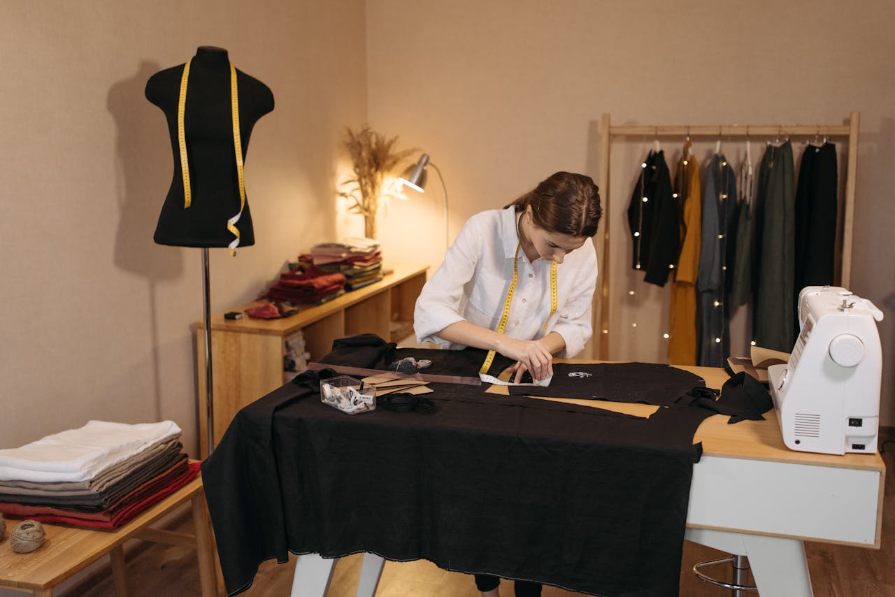 about-us A woman involved in dressmaking tasks in a studio, measuring and cutting fabric.