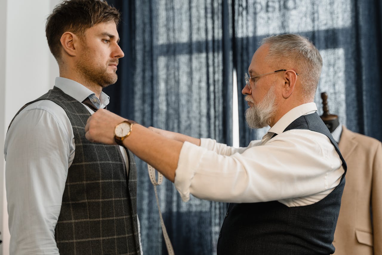 home-hero Professional tailor measuring a client for a custom suit in a workshop setting.
